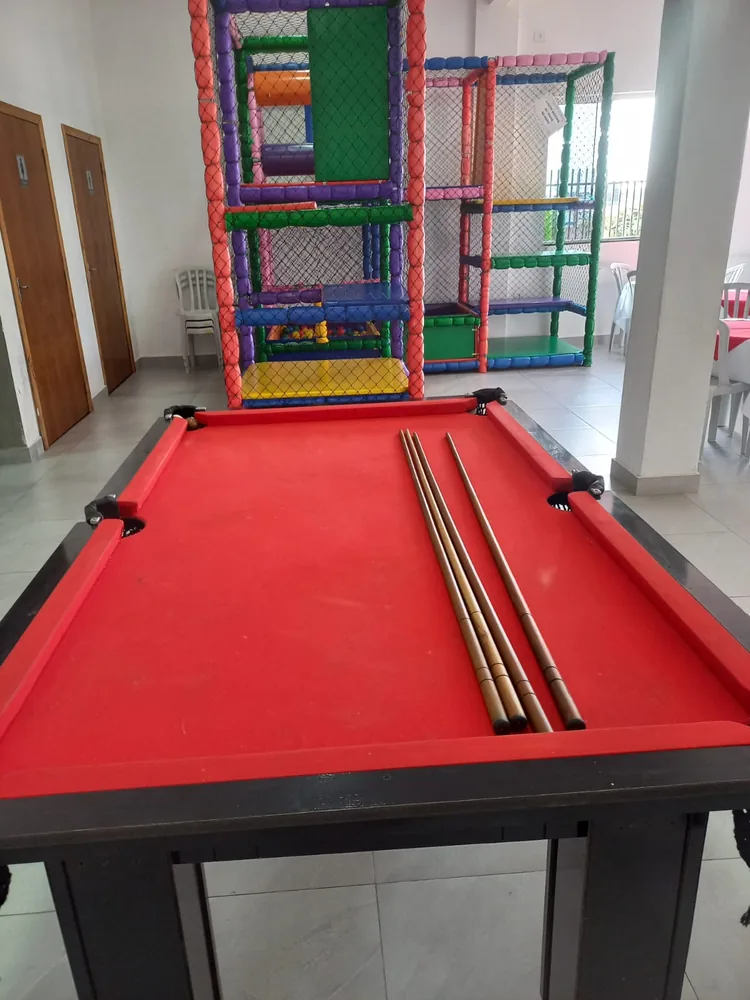Mesa de sinuca vermelha com tacos e playground ao fundo